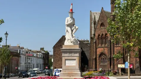 The Rabbie Burns statue in Dumfries with a traffic cone on its head.