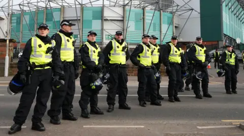 PA A row of police officers wearing hi-viz vests lined up outside Celtic Park