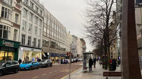 BBC A generic shot of Belfast city centre, royal avenue area... Rows of shops with cars parked on pavements