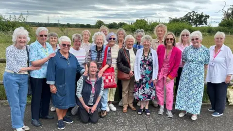 Kay Crewdson, fourth from right, is standing with a group of about 20 women from Barnston Women's Institute. All smiling, they are huddled together for the photograph.