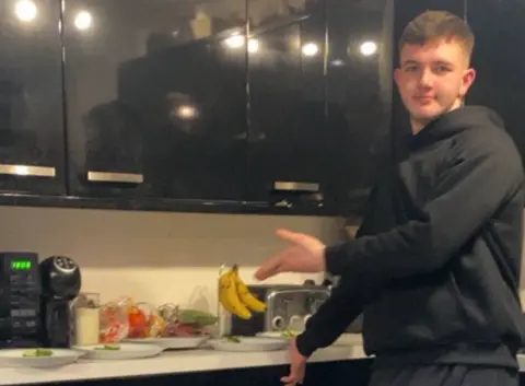 Police Scotland Cole Coopper is wearing a black sweatshirt and is standing in a kitchen point to some plates of food