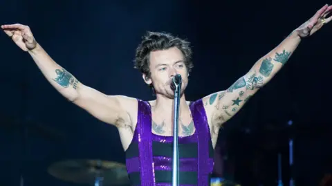 Harry Styles stands on stage at Radio 1's Big Weekend at the War Memorial Park in Coventry in 2022 wearing a black sleeveless top with purple sequin details
