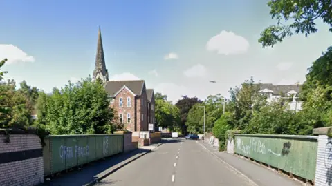 Google A green bridge with white graffiti on the side of Rock Lane West with a block of flats in the distance