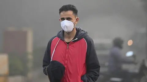 Getty Images A man wearing a pollution mask and a red-and-black wind cheater among commuters seen moving through dense smog on a cold morning near MDI Institute in Delhi suburb Gurugram on 14 December