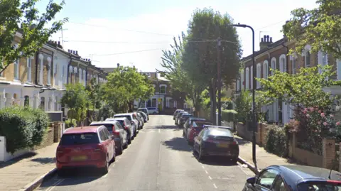 Residential road lined with houses with cars parked along either side of the street