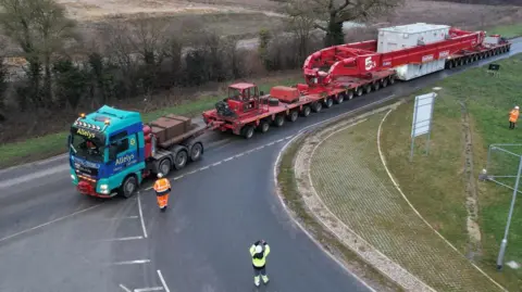 Orsted An abnormal load being escorted on a red trailer. It is travelling along a single carriageway road.