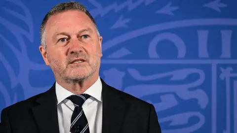 Getty Images Housing Secretary Steve Reed speaking against a blue government backdrop featuring the royal crest.