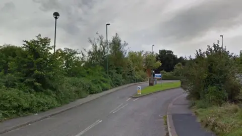 A road leading up to the entrance of the Reaside Clinic. There is a blue and white sign identifying the site.