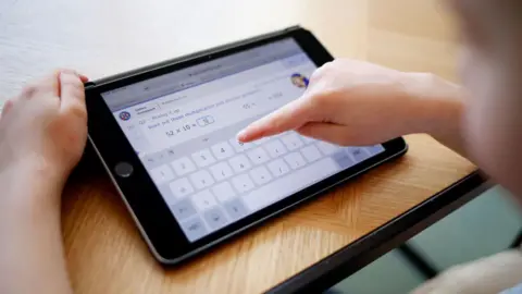 A student, blurred in the picture, uses an iPad for school work. 