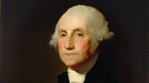 Getty Images A painting of George Washington. He is sat sideways and looking at the painter. He is wearing a white scarf and black jacket against a brown background. He has mid-length grey hair.
