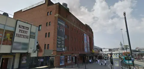 Google Exterior of Liverpool's Royal Court theatre, a red brick building with large poster advertising performances on the front 