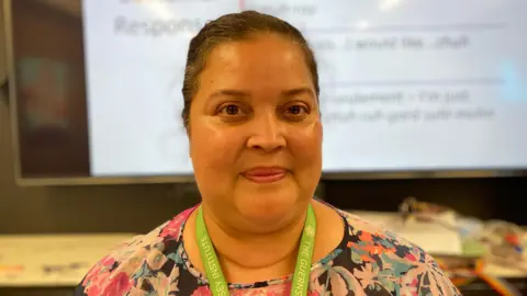 A women smiling at the camera. She has dark hair that is scraped back. She is wearing a lime green lanyard that says The Guernsey Institute along it.