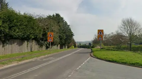 Google A Google street view image showing a rural road with two road signs either side of it. 