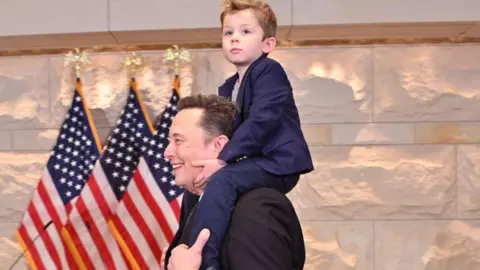 Getty Images Tesla CEO Elon Musk, co-chair of the newly created Department of Government Efficiency (DOGE), carries his son "X" on his shoulders before a meeting with members of Congress at the US Capitol on 5 December 