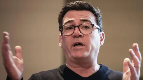 PA Andy Burnham gestures with his hands held at shoulder width as he gives a speech while wearing a black top.