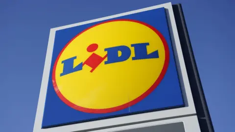 The supermarket logo consists of a yellow circle with a red border that sits on a blue background. The word "Lidl" is written in blue, uppercase letters, with the exception of the "i" which is red and slightly tilted.
