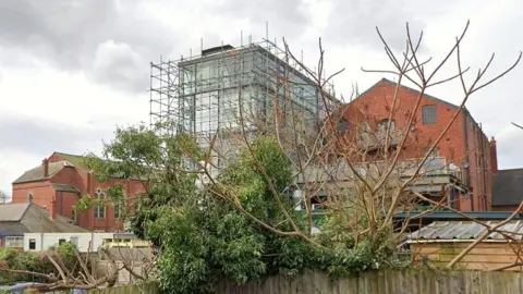 The rear of Jacob's Court is covered in scaffolding with other buildings surrounding it. 