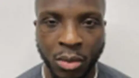 Blurry custody photo of a man. He is wearing a grey T-shirt.