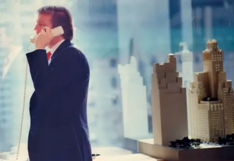 Getty Images Donald Trump makes a phone call at his Trump Plaza office in Manhattan in 1987. There is a model of a skyscraper development beside him.