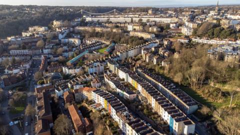 An aerial view of Bristol showing colourful houses in the foreground and the Clifton Suspension Bridge in the background