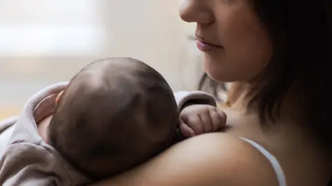 A woman with shoulder-length brown hair cradles a baby (stock image) 
