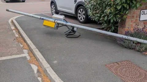 A lamppost, knocked over, with a speed camera attached to it.