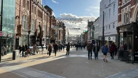 A wide shot of Briggate in Leeds - a wide, paved pedestrian street lined with shops on both sides.