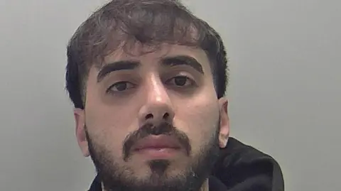 Warwickshire Police Mugshot of Mohammed, who is wearing a black hoodie and has short black hair, a moustager and a beard