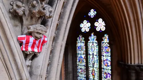 Harry Parkhill / BBC The Lincoln Imp wearing the club's shirt it sits on the top of a stone column with a stained glass window in the background