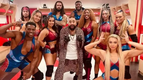 BBC/Comic Relief 2025/Colin Hopkins Chabuddy G actor Asim Chaudhry surrounded by the cast of Gladiators
