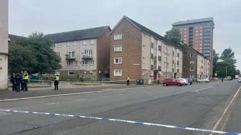 Police cordon around a block of flats in Paisley. Officers stand inside the cordon.