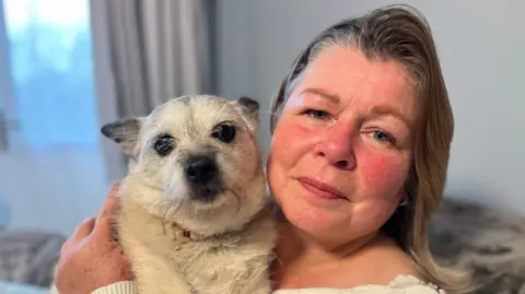 Teresa holding Morgan's white small dog Peaches. Teresa has shoulder-length fair hair. 