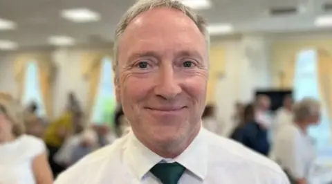 Man with grey hair and in a shirt and tie