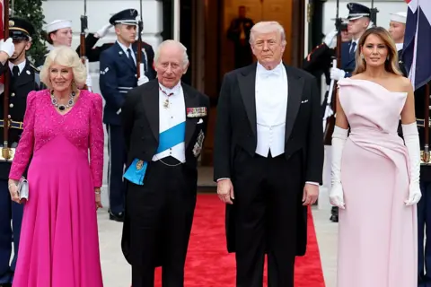 Queen Camilla, King Charles III, U.S. President Donald Trump, and First Lady Melania Trump pose at the base of the Grand Staircase during an official state dinner hosted by the President and First Lady at The White House on day two of the State Visit