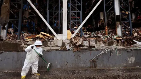 A worker helps clean up the site of the massive Lineage warehouse fire along Union Pacific Avenue in the Boyle Heights on June 30, 2026. Signal Restoration Services is a national emergency cleanup and property damage firm. The stench from millions of pounds of rotting food spread through the neighborhood and city officials and neighborhood residents look to hold those responsible for the fire and its aftermath accountable. Lineage has begun the colossal task of removing an estimated 85 million pounds of spoiled food from the facility