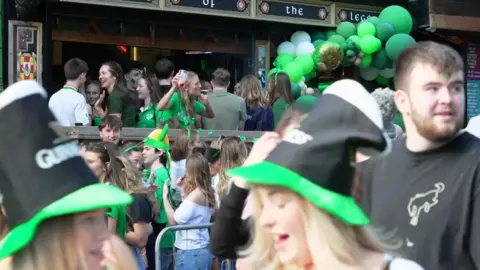 People cram an Irish bar with green balloons.