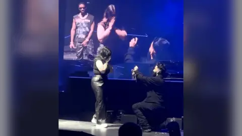 A man proposes to a woman on a stage in the O2 arena.