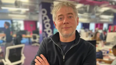 Octopus energy boss Greg Jackson looks at camera, wearing black zip-up sweatshirt and dark t-shirt