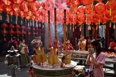 Lillian Suwanrumpha/AFP A woman prays near to burning incense underneath red lanterns