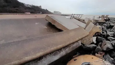 A concrete path by the sea which has been torn apart by a storm.