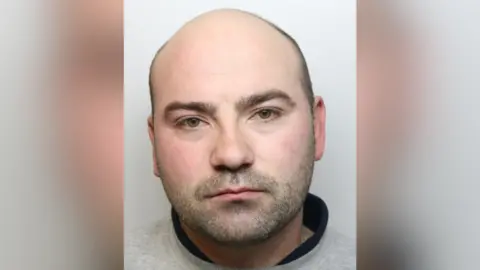 A police mug shot of Russel Thornton who is a white man with very short hair and beard stubble.