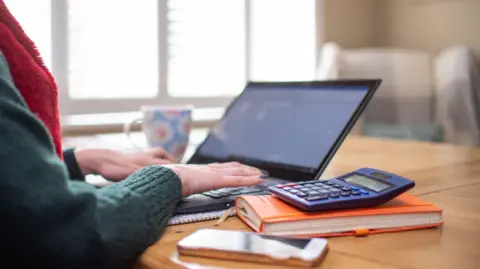 PA Media A woman using a laptop on a dining room table set up as a remote office to work from home.