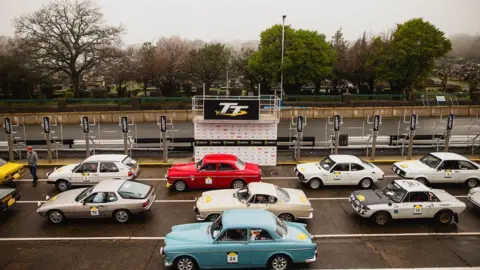 WILL BROADHEAD Classic Cars line up at the pit lane at the Grandstand, you can see a banner which says TT in the background.