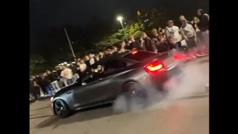 SNAP Footage from the car meet of a black car skidding its tyres in front of a large crowd.