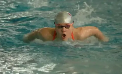 A person's head in a silver swimming cap emerging from the water of a swimming pool