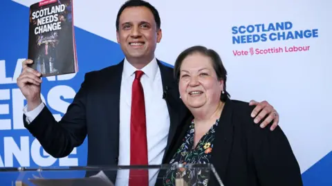 Two people, man and woman, at podium holding up a political manifesto
