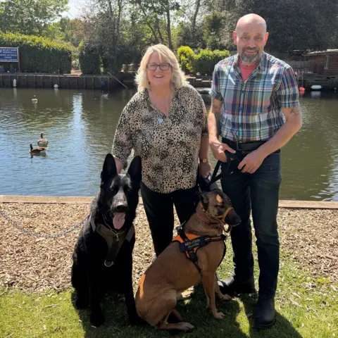 Supplied A photograph of two people, a woman and a man, smiling while stood next to two dogs
