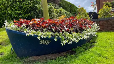 Andrew Turner/BBC A blue boat filled with flowers on a lawn.