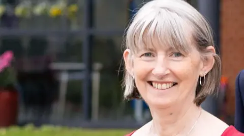 Rogan Productions Tina a woman with grey hair and a fringe is smiling next to her husband Mark who has grey hair and wears a blue shirt and jacket 