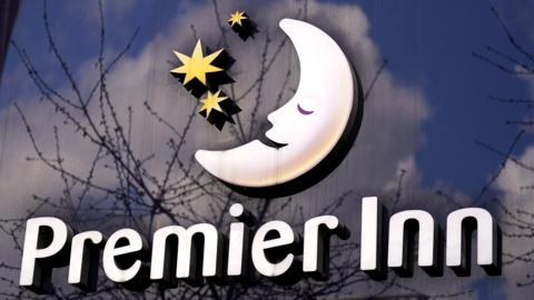 Premier Inn sign on a reflective glass background incorporating a crescent moon with a smiling face next to three yellow stars